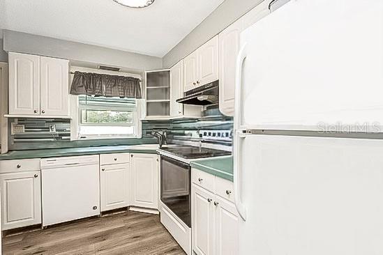 kitchen with under cabinet range hood, white appliances, wood finished floors, white cabinets, and backsplash