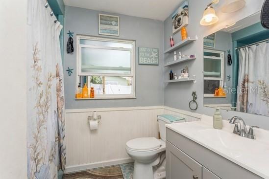 full bath featuring curtained shower, wainscoting, vanity, and toilet