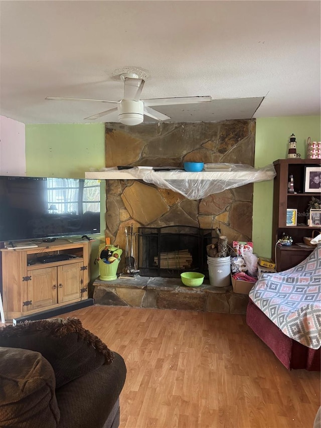 living room with ceiling fan, a stone fireplace, and wood finished floors