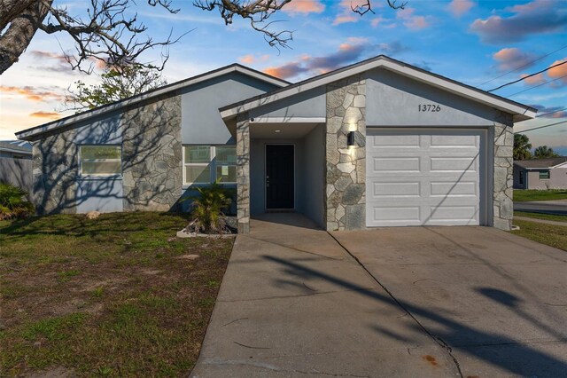 mid-century inspired home with stone siding, an attached garage, driveway, and stucco siding