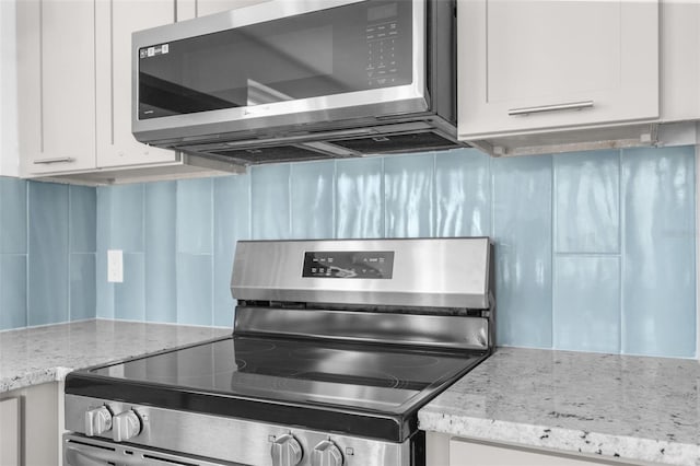 kitchen featuring appliances with stainless steel finishes, white cabinetry, light stone counters, and tasteful backsplash