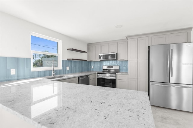 kitchen featuring light stone counters, gray cabinetry, stainless steel appliances, a sink, and tasteful backsplash