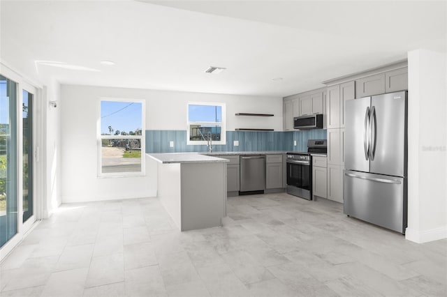 kitchen with appliances with stainless steel finishes, a sink, gray cabinetry, and open shelves