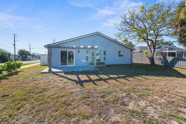 rear view of house featuring a patio, a lawn, fence, and stucco siding