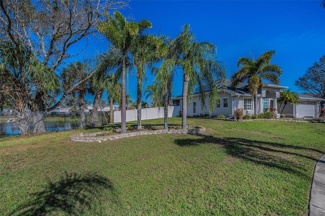 view of yard with an attached garage, fence, and a water view