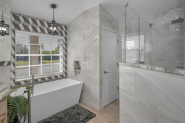 bathroom with tile walls, a stall shower, wood finished floors, a chandelier, and a freestanding tub