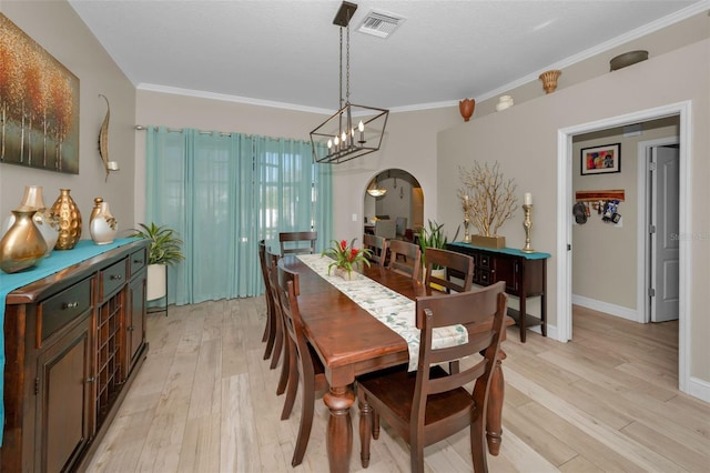 dining room featuring visible vents, arched walkways, baseboards, crown molding, and light wood-style floors