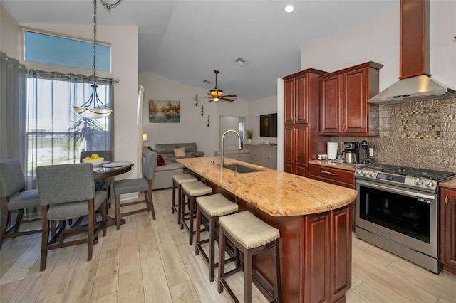 kitchen with a sink, stainless steel gas range, backsplash, reddish brown cabinets, and wall chimney exhaust hood