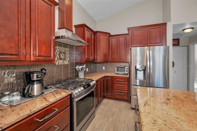 kitchen with light stone counters, stainless steel appliances, vaulted ceiling, dark brown cabinets, and wall chimney range hood