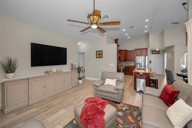 living area featuring high vaulted ceiling, light wood finished floors, visible vents, and a ceiling fan