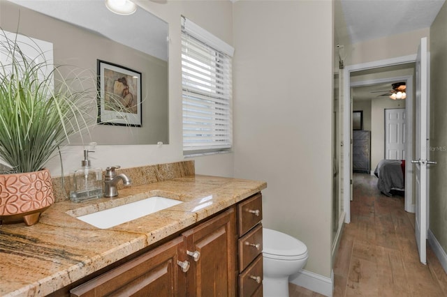 ensuite bathroom featuring a ceiling fan, connected bathroom, toilet, wood finished floors, and vanity