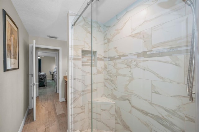 bathroom featuring a marble finish shower, visible vents, a textured ceiling, wood finished floors, and baseboards