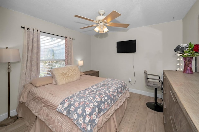 bedroom featuring ceiling fan, a textured ceiling, light wood-type flooring, and baseboards