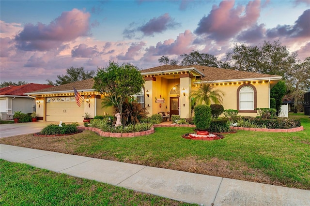 mediterranean / spanish house featuring an attached garage, concrete driveway, a lawn, and stucco siding