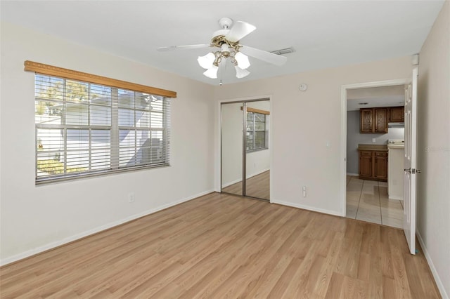 unfurnished bedroom featuring light wood-type flooring, visible vents, a ceiling fan, a closet, and baseboards