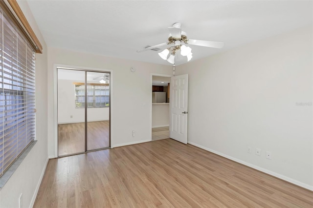 unfurnished bedroom featuring a ceiling fan, wood finished floors, baseboards, freestanding refrigerator, and a closet