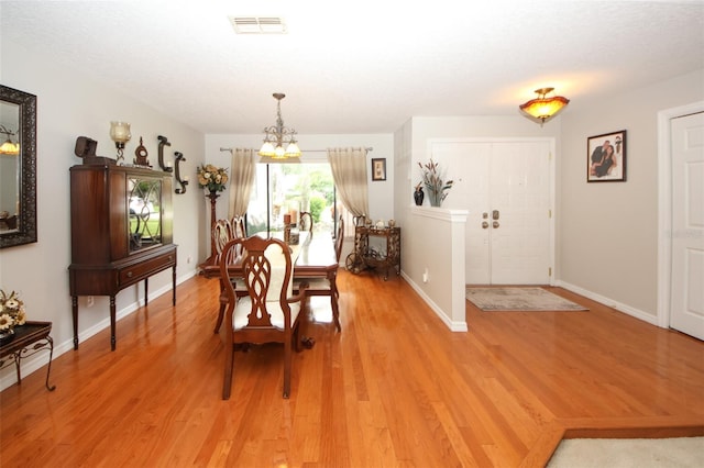 dining area with a chandelier, baseboards, visible vents, and light wood finished floors