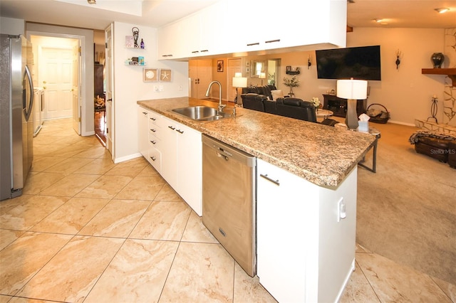 kitchen featuring stainless steel appliances, open floor plan, white cabinets, a sink, and a peninsula