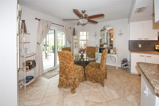 dining space featuring light tile patterned floors, visible vents, arched walkways, ceiling fan, and a textured ceiling