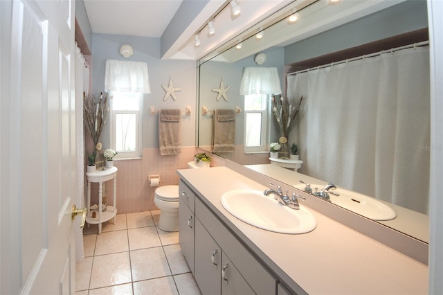 bathroom with a wainscoted wall, plenty of natural light, tile walls, and tile patterned floors