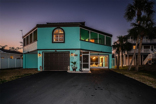 view of front facade featuring stucco siding, driveway, an attached garage, and fence