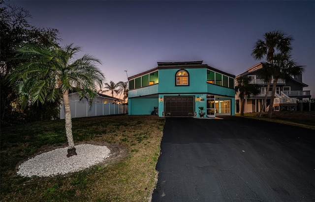 view of front of house featuring an attached garage, fence, driveway, a yard, and stucco siding