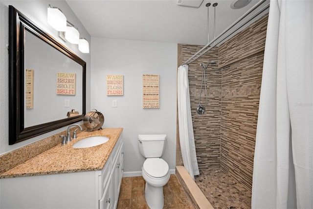 bathroom with toilet, baseboards, tiled shower, and vanity