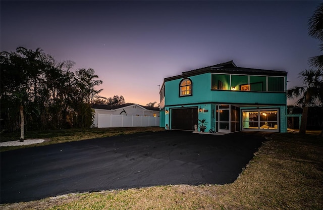 rear view of house with driveway, a garage, and fence