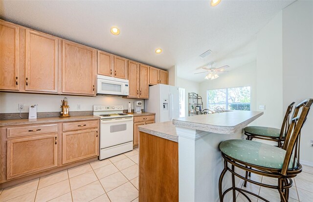 kitchen featuring light brown cabinets, light tile patterned floors, a kitchen breakfast bar, white appliances, and a ceiling fan