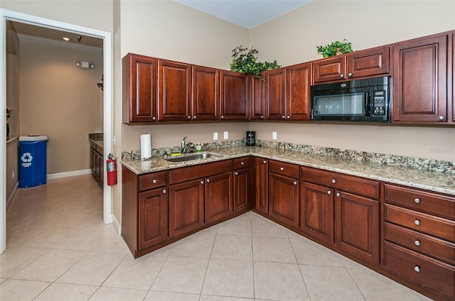 kitchen with light stone counters, light tile patterned flooring, black microwave, and a sink