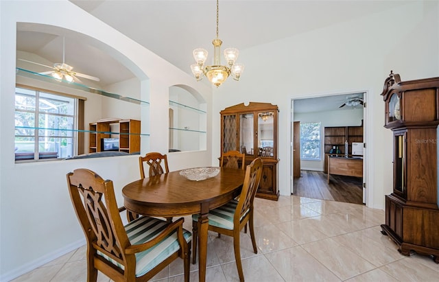 dining area featuring light tile patterned floors, baseboards, arched walkways, vaulted ceiling, and ceiling fan with notable chandelier