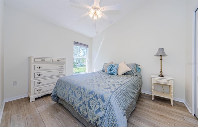 bedroom featuring light wood finished floors, ceiling fan, baseboards, and vaulted ceiling