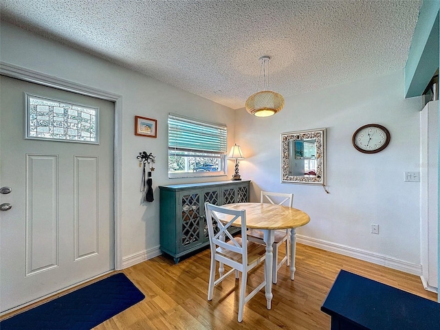 dining room featuring a textured ceiling, light wood finished floors, and baseboards