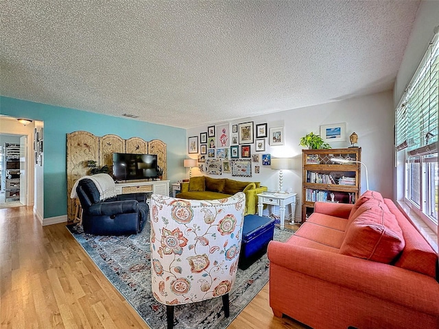 living room featuring visible vents, a textured ceiling, baseboards, and wood finished floors