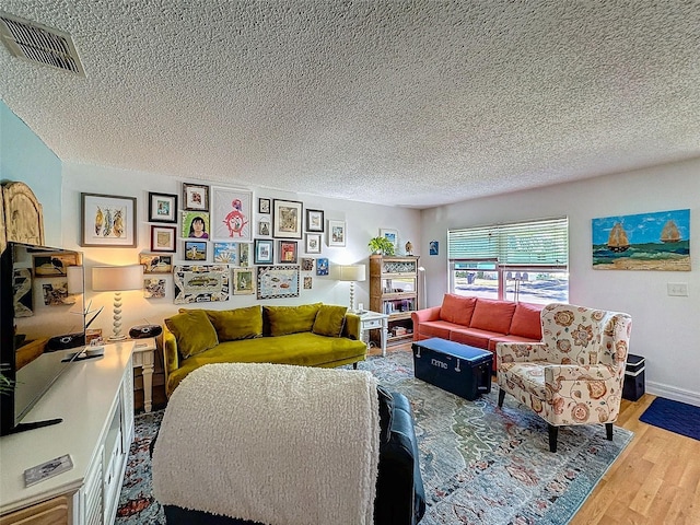 living area with baseboards, a textured ceiling, visible vents, and wood finished floors