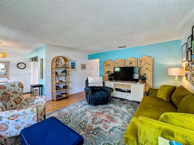 living area featuring baseboards, a textured ceiling, visible vents, and wood finished floors