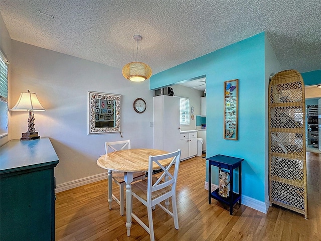 dining space featuring light wood-style flooring, baseboards, and a textured ceiling