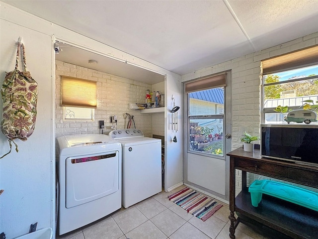 washroom with laundry area, brick wall, light tile patterned floors, and washer and clothes dryer