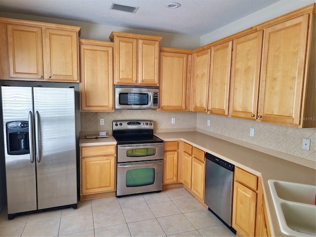 kitchen with light tile patterned floors, stainless steel appliances, light countertops, and visible vents