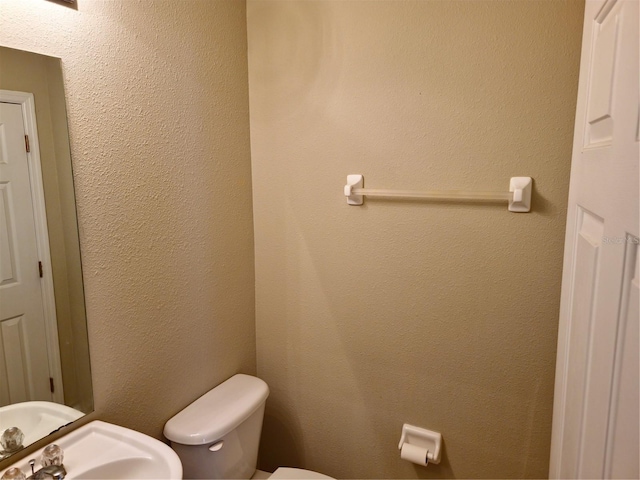 half bath with a textured wall, a sink, and toilet