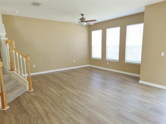 unfurnished room with light wood finished floors, visible vents, ceiling fan, baseboards, and stairs