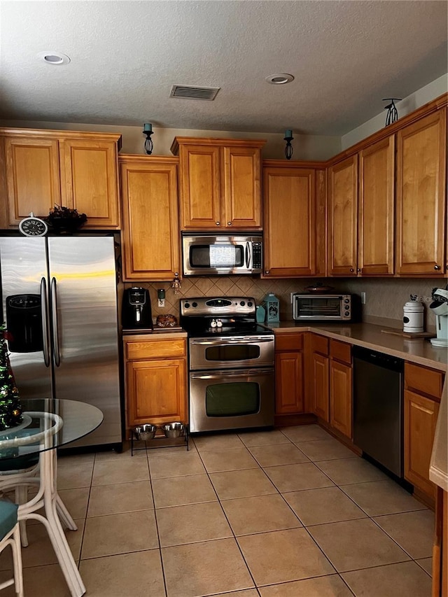 kitchen with light tile patterned floors, appliances with stainless steel finishes, brown cabinetry, and visible vents