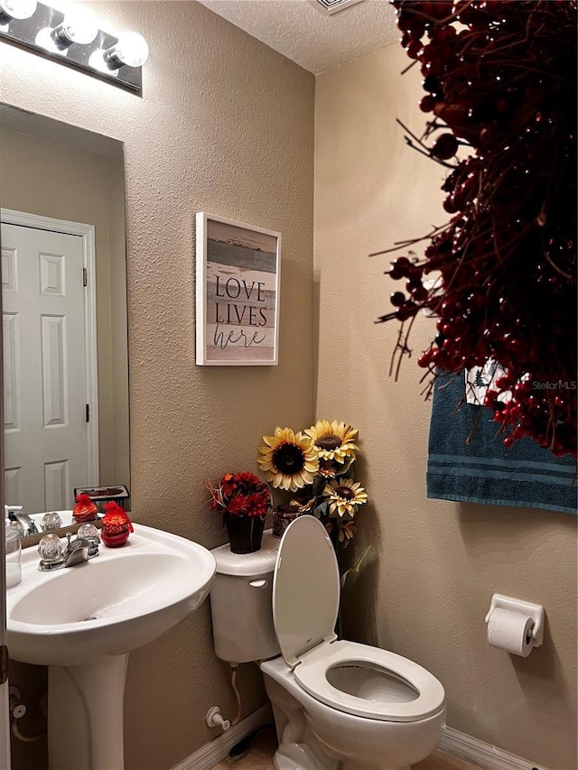 bathroom featuring toilet, baseboards, and a textured ceiling