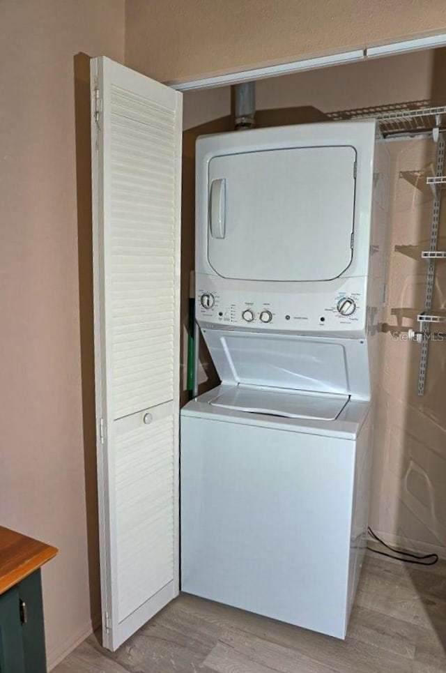 clothes washing area featuring light wood-type flooring, stacked washer / drying machine, and laundry area