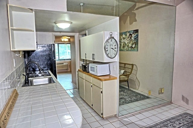 kitchen featuring light tile patterned floors, visible vents, tile countertops, white microwave, and a sink