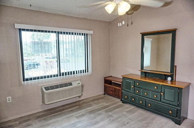 bedroom featuring a textured ceiling, a wall unit AC, a ceiling fan, baseboards, and light wood finished floors