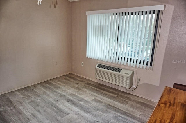 empty room with a wall unit AC, baseboards, and wood finished floors