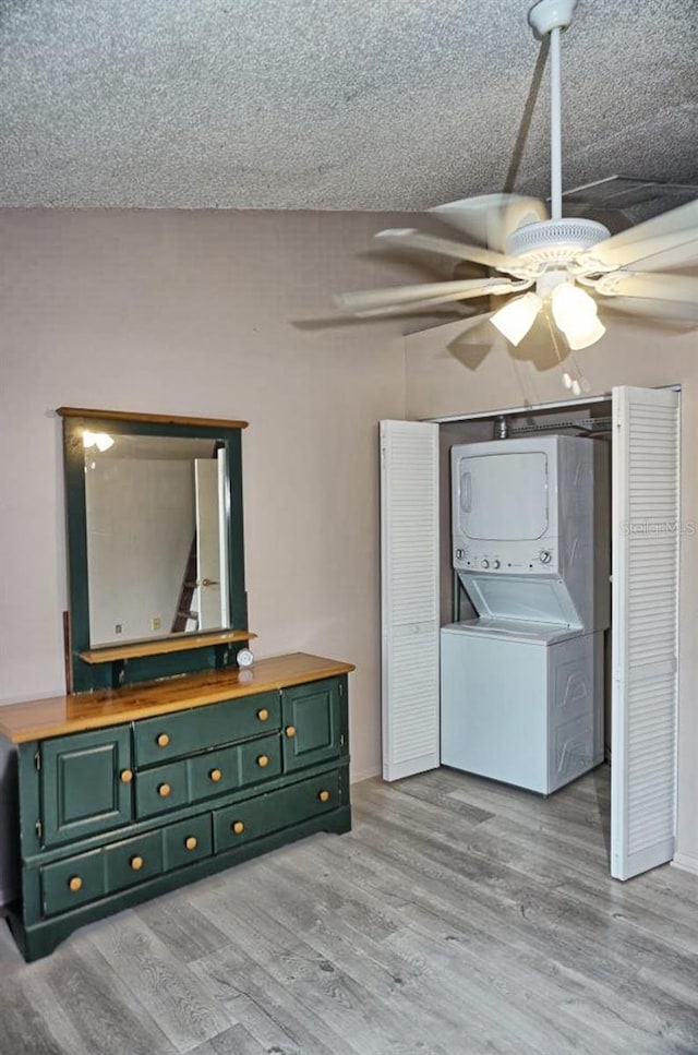 interior space with a textured ceiling, wood finished floors, a ceiling fan, and stacked washer / drying machine