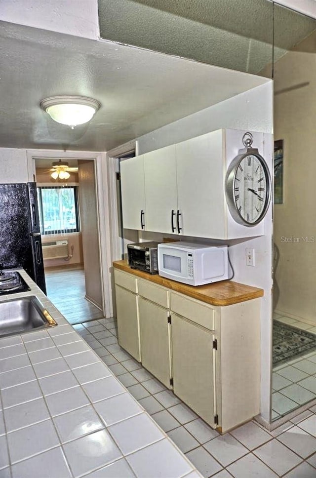 kitchen with light tile patterned floors, tile countertops, white microwave, freestanding refrigerator, and a textured ceiling