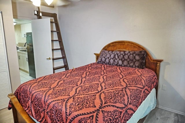 bedroom featuring freestanding refrigerator, ensuite bathroom, a ceiling fan, and wood finished floors